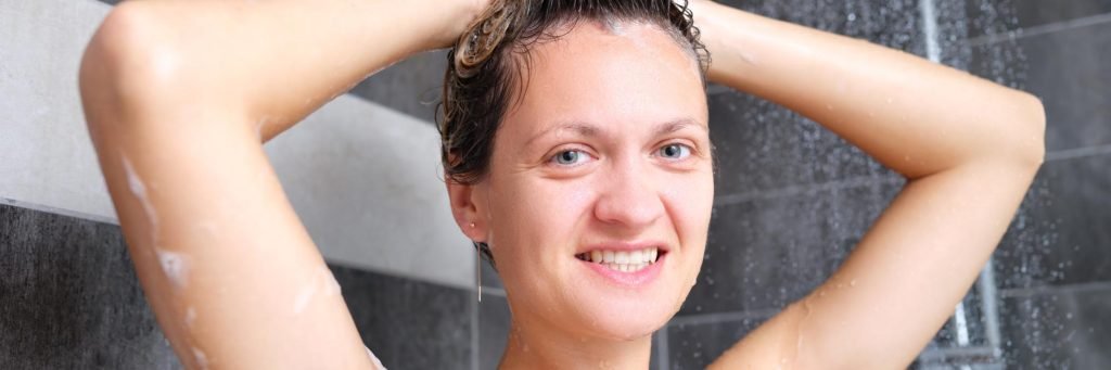joven hermosa mujer bajo la ducha en el baño despues de hacerse una exfoliación con exfoliantes físicos