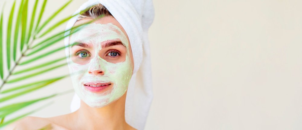 hermosa mujer con una máscara de peeling enzimático facial verde y una toalla en la cabeza