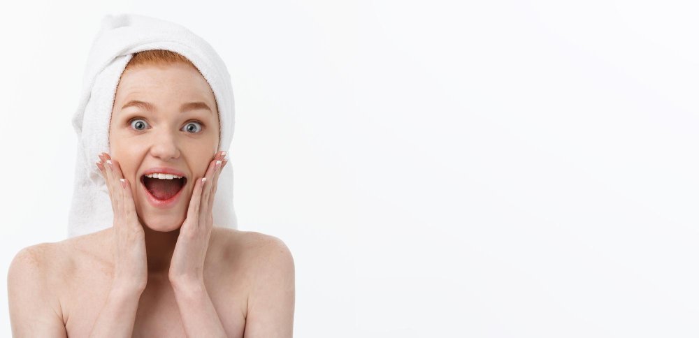 sorprendida hermosa mujer joven después del baño con una toalla en la cabeza aislada sobre fondo blanco, después de su exfoliación