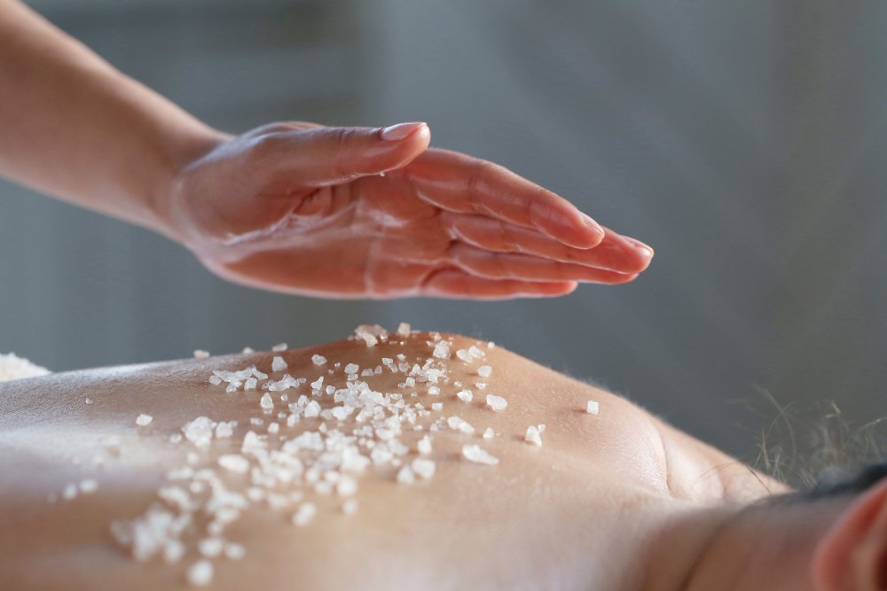 mujer desnuda de espalda con exfoliante y mano aplicandolo